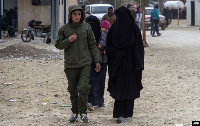 FILE - A Kurdish female fighter, left, walks next to a woman, reportedly the wife of an Islamic State (IS) group fighter, at the Internally Displaced Persons (IDP) camp of al-Hol in al-Hasakeh governorate in northeastern Syria, Feb. 7, 2019.