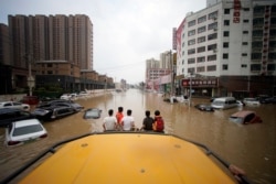 People ride a front loader as they wade through a flooded road following heavy rainfall in Zhengzhou, Henan province, China July 22, 2021
