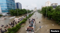 People sit atop a bus roof while others wade through the flooded road during monsoon rain, as the outbreak of the coronavirus disease (COVID-19) continues, in Karachi, Pakistan August 27, 2020. 