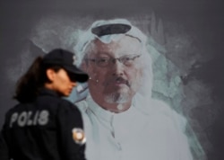 FILE - A Turkish police officer walks past a picture of slain Saudi journalist Jamal Khashoggi prior to a ceremony, near the Saudi Arabia consulate in Istanbul, marking the one-year anniversary of his death, Oct. 2, 2019.