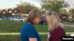 Beverly Turner and Michele Brown huddle to pray in front of a fence decorated with wreaths as students and faculty arrive at Marjory Stoneman Douglas High School for the first time since the mass shooting in Parkland, Florida, Feb. 28, 2018. 