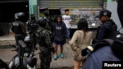 Oficiales de la Policía Militar revisan a las personas mientras reclusos (no aparecen en la foto) pintan sobre graffitis como parte de un programa gubernamental para promover la inserción social a través del trabajo comunitario, en Tegucigalpa, Honduras, el 9 de julio de 2024.