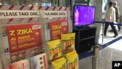 People walk past a travel advisory on the Zika virus infection in Kuala Lumpur International Airport in Sepang, Malaysia, Aug. 28, 2016. 