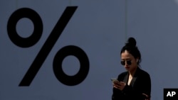 FILE - A woman wears Apple AirPods while browsing her iPhone at a popular shopping mall in Beijing, April 4, 2019. 