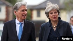 FILE - Britain's Prime Minister Theresa May and Chancellor of the Exchequer Philip Hammond visit a home near the Conservative Party's conference in Manchester, Oct. 2, 2017.