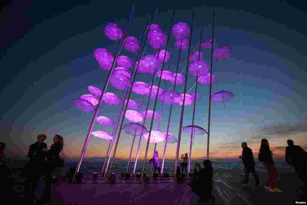 People stand around "Umbrellas", the sculpture by Giorgos Zogolopoulos, as it is illuminated in pink light to mark the Breast Cancer Awareness Month in Thessaloniki in northern Greece, Oct. 21, 2014.