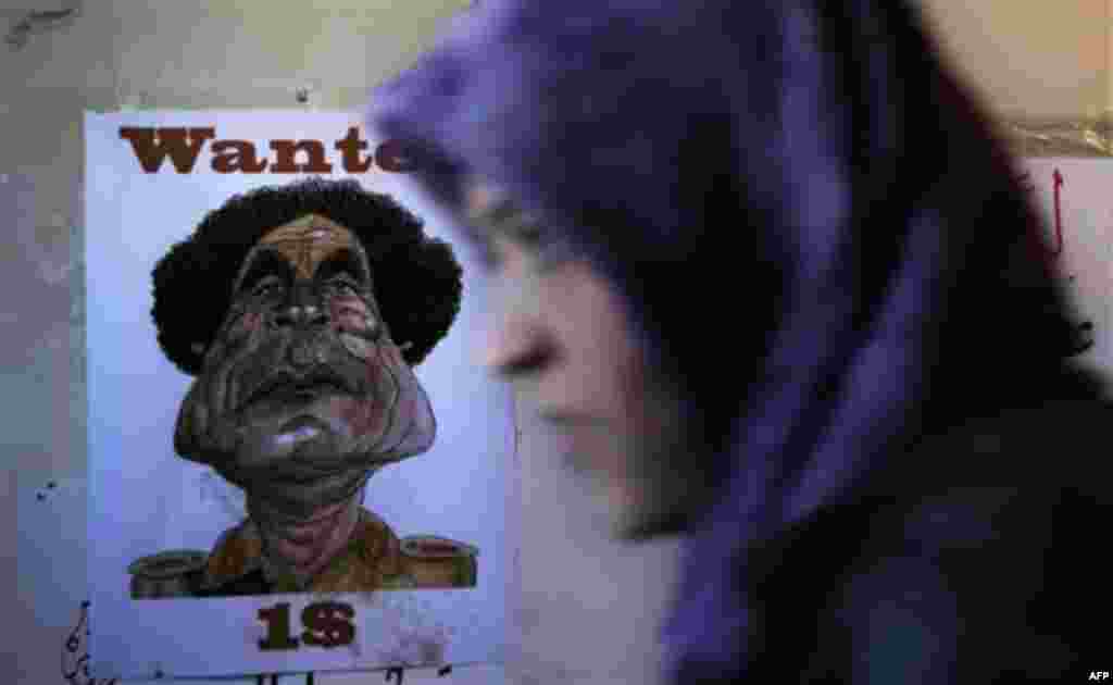 A Libyan woman passes an anti-Gadhafi wanted poster with his picture during the ongoing protest at the Tahrir square in Benghazi, Libya Saturday, March 12, 2011. Moammar Gadhafi tightened his grip Saturday on the coastal road linking his territory to the