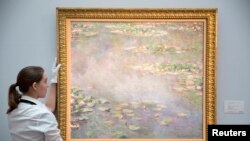 Une assistante de gallerie pose le tableau Nympheas de Claude Monet lors d'une photo-call pour la vente d'art à la maison de ventes Sotheby's à Londres le 18 juin 2014. REUTERS / Neil Hall