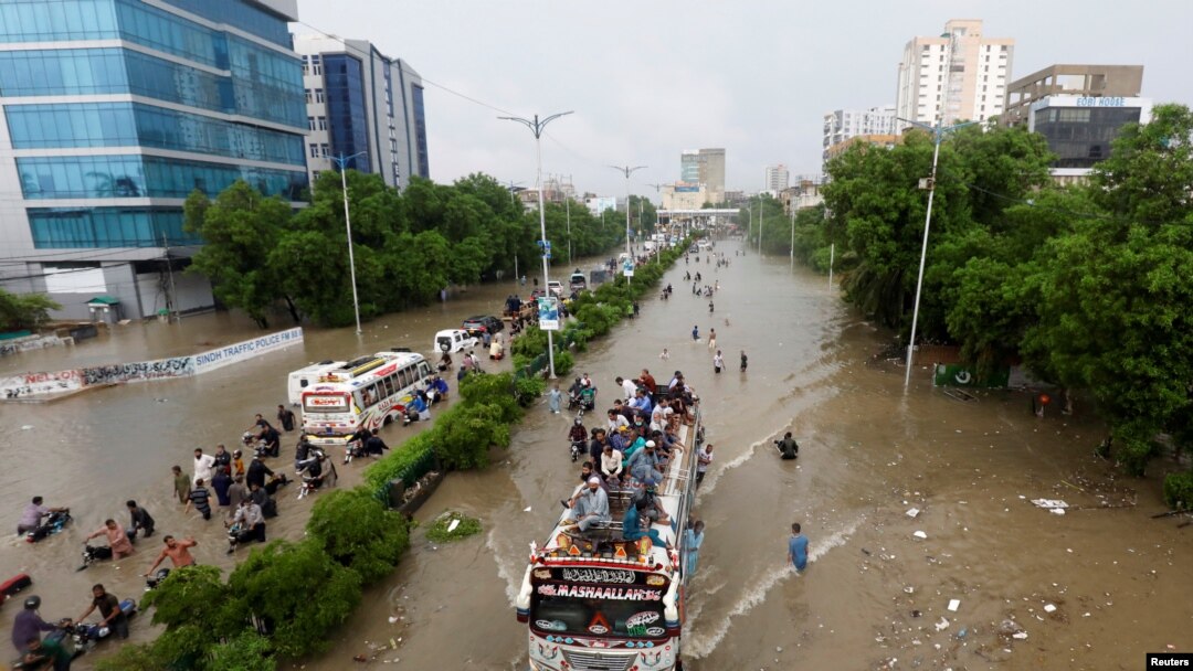 People sit atop a bus roof while others wade through the flooded road during monsoon rain, as the outbreak of the coronavirus disease (COVID-19) continues, in Karachi, Pakistan August 27, 2020. 