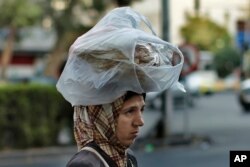 FILE - A woman carries bread on her head while she crosses a street in Damascus, July 24, 2019. After nearly a decade of war, Syria is crumbling under the weight of sanctions, government coruption and other problems.