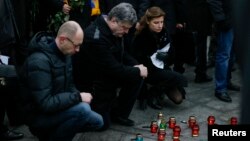 El presidente de Ucrania, Petro Poroshenko (centro) y su esposa Marina, junto al Primer Ministro Arseny Yatseniuk (izquierda) encienden velas durante marcha en Kiev, el domingo, 18 de enero, de 2015. 