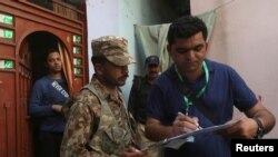 A census enumerator (R) along with a Pakistan Army soldier notes details outside a house