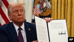 President Donald Trump holds up a signed executive order relating to the Lumbee Tribe of North Carolina in the Oval Office of the White House, Thursday, Jan. 23, 2025, in Washington. (AP Photo/Ben Curtis)