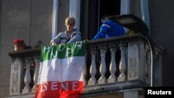 Une femme place un drapeau italien qui proclame que "tout ira bien", du balcon de son appartement où elle est confinée à Milan, Italie, le 16 mars 2020. REUTERS / Daniele Mascolo
