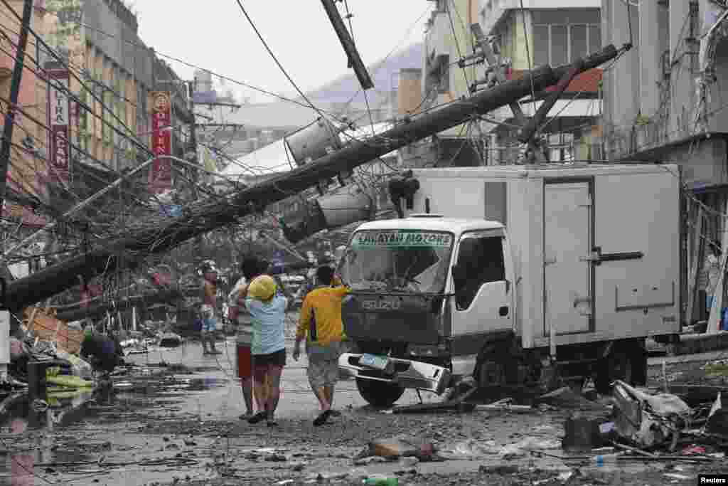 Survivors walk under a fallen electric post after super Typhoon Haiyan battered Tacloban city, central Philippines. 