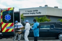 FILE - Emergency Medical Technicians (EMT) arrive with a patient while a funeral car begins to depart at North Shore Medical Center where the coronavirus disease (COVID-19) patients are treated, in Miami, Florida, July 14, 2020.