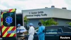 FILE - Emergency Medical Technicians (EMT) arrive with a patient while a funeral car begins to depart at North Shore Medical Center where the coronavirus disease (COVID-19) patients are treated, in Miami, Florida, July 14, 2020. 