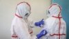 FILE - A nurse writes on the protective clothing of fellow nurse Lucy Kanyi, right, with her name so she can be recognized when wearing it and the time of day, at the infectious disease unit of Kenyatta National Hospital, Nairobi, Kenya, March 6, 2020.