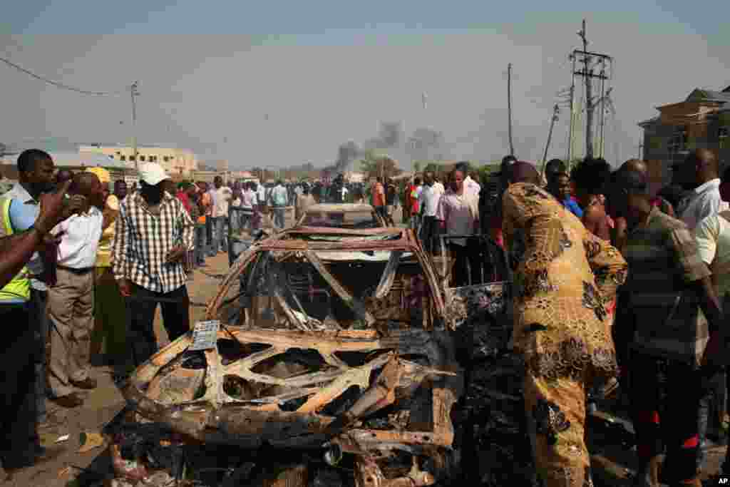 Onlookers stand by a destroyed car at the site of a bomb blast at St. Theresa Catholic Church in Madalla, Nigeria. (AP)