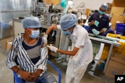 Un agent de santé indien administre le vaccin Covishield pour COVID-19 à un travailleur de l'usine d'un fabricant de masques faciaux à la périphérie d'Ahmedabad, en Inde, le 17 décembre 2021.