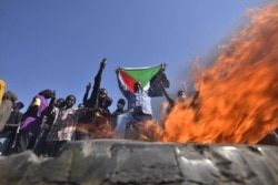 A man holds a Sudanese national flag before flames at a barricade as people protest against the military coup in Sudan, in 'Street 60' in the east of capital Khartoum on Nov. 13, 2021.