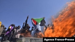 Un homme tient un drapeau national soudanais devant les flammes d'une barricade alors que les gens protestent contre le coup d'État militaire au Soudan, dans la "rue 60" à Khartoum, le 13 novembre 2021.