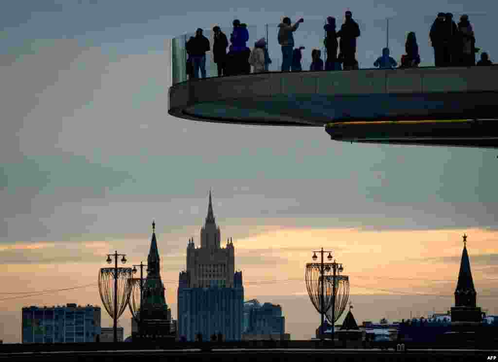 Warga menikmati pemandangan dari jembatan penyeberangan di Taman Zaryadye, dengan latar belakang menara Kremlindi Moskow, Rusia.