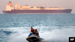 In this Friday, July 26, 2019 file photo, a ship crosses the Gulf of Suez towards the Red Sea as holiday-makers ride a jet ski at al Sokhna beach in Suez, 127 kilometers (79 miles) east of Cairo, Egypt. (AP Photo/Amr Nabil)