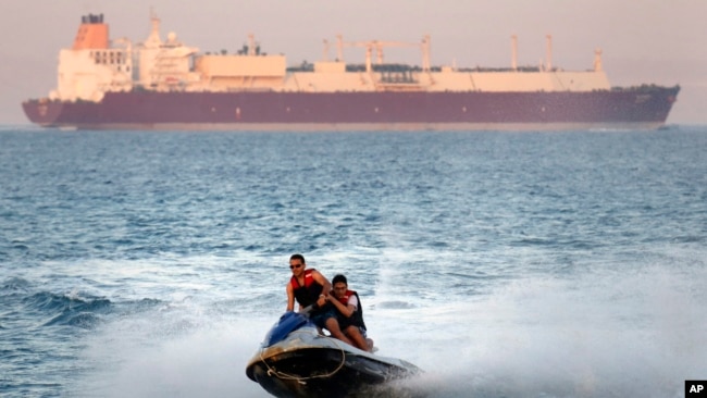 In this Friday, July 26, 2019 file photo, a ship crosses the Gulf of Suez towards the Red Sea as holiday-makers ride a jet ski at al Sokhna beach in Suez, 127 kilometers (79 miles) east of Cairo, Egypt. (AP Photo/Amr Nabil)