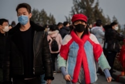 A couple wears masks to help stop the spread of a deadly virus as they walk at Jingshawn park, in Beijing, Jan. 25, 2020. China said it would close a section of the Great Wall and other famous Beijing landmarks to control the spread of the virus.