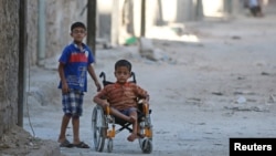 FILE - Boys, one of them in a wheelchair, venture down a street in the al-Sheikh Said neighborhood of Aleppo, Syria, Sept. 1, 2016. 