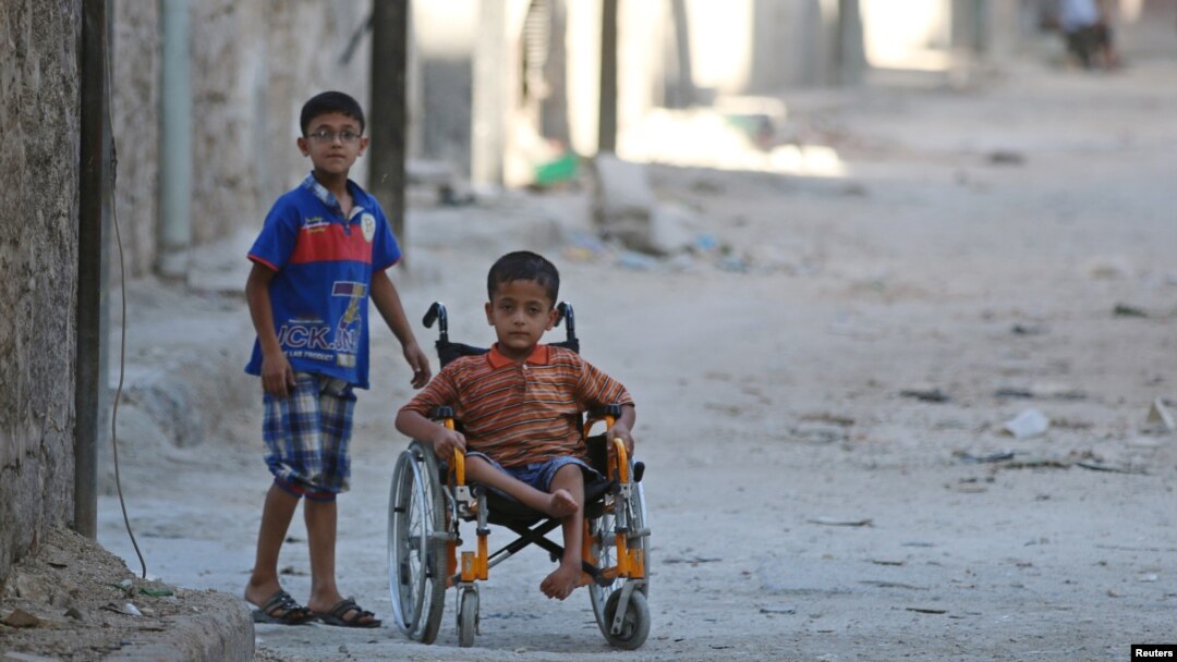 FILE - Boys, one of them in a wheelchair, venture down a street in the al-Sheikh Said neighborhood of Aleppo, Syria, Sept. 1, 2016. 