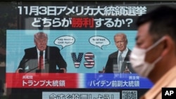 FILE - A man walks past a screen showing illustrations of President Donald Trump, left, and former Vice President Joe Biden for an online voting to predict the winner in the U.S. presidential election, in Tokyo, Oct. 26, 2020. 