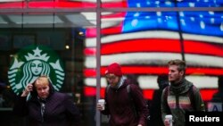 A woman pulls a hood over her head as she walks out of a Starbucks store into the cold wind at Times Square in New York, March 25, 2013.