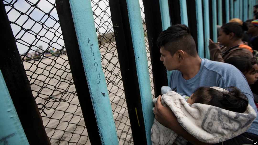 ARCHIVO - Un integrante de una caravana de migrantes de Centroamérica mira a través de una barrera en la frontera sur de Estados Unidos en Tijuana, México, el 29 de abril de 2018.