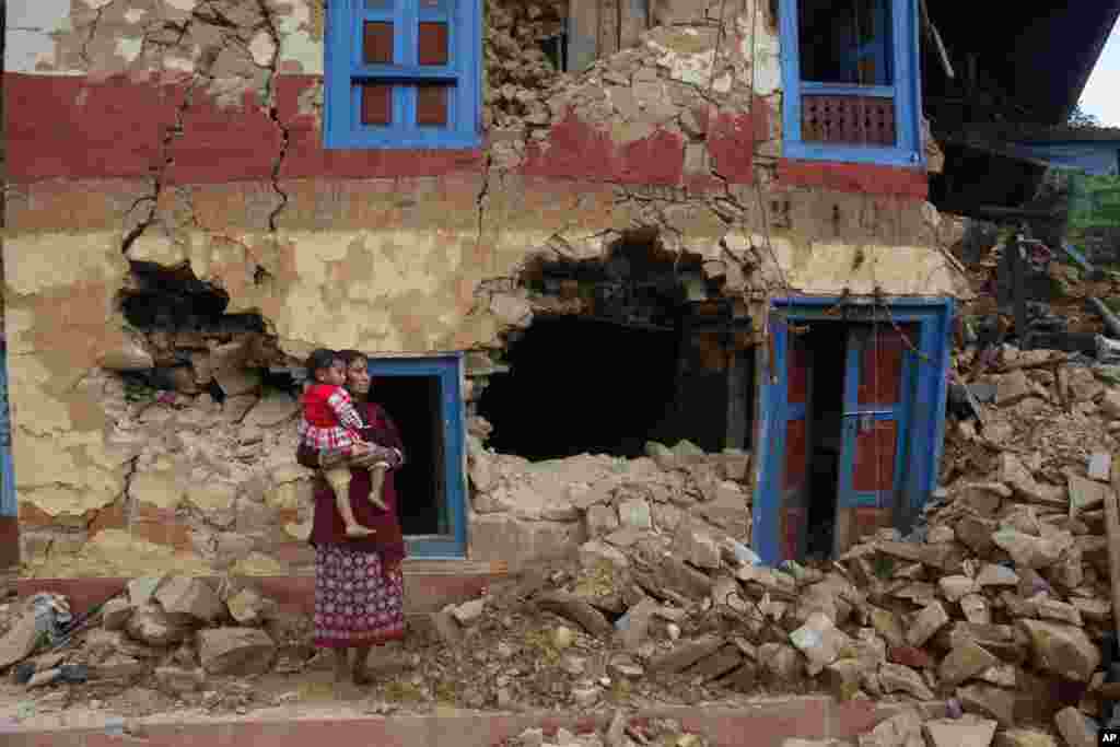 A Nepalese woman carries her child outside her house damaged in last month&rsquo;s earthquake on the outskirts of Lalitpur, Nepal.