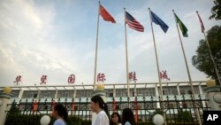 In this June 6, 2017, photo, Chinese, American, and other international flags fly as women walk past a Huajian Group shoe factory, the one time shoe maker for the Ivanka Trump brand, in Ganzhou in southern China's Jiangxi Province.