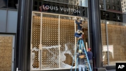 Trabajadores cubren con madera un escaparate de la tienda Louis Vuitton que fue destruído por vándalos y saqueadores en la noche del domingo y madrugada del lunes. Los saqueadores hicieron destrozos en la exclusiva zona de la Magnífica Milla de Chicago.