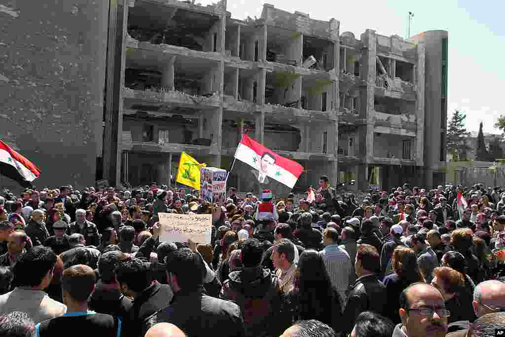Thousands of people wave Syrian flags during a silent march in front of a damaged government building on al-Qassa street in Damascus in memory of people who were killed in explosions one day earlier. (AP)