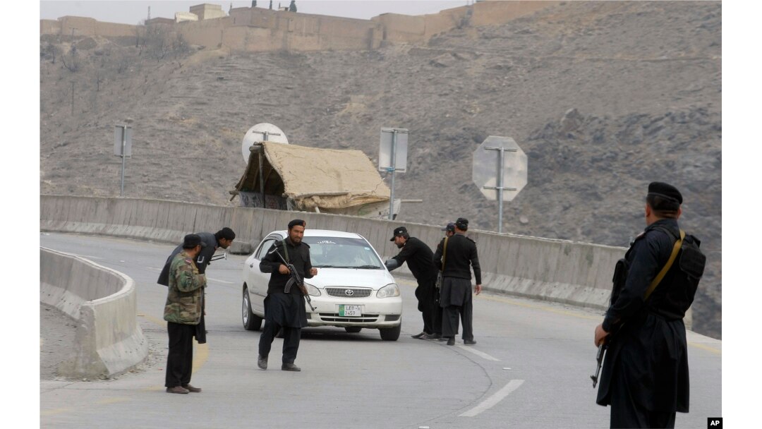 Pakistani police officers stand guard while their colleagues searching a car at a checkpoint on the highway leading to Torkhum, a border crossing between Pakistan and Afghanistan, March, 20, 2017.
