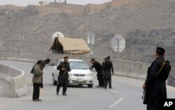 Pakistani police officers stand guard while their colleagues searching a car at a checkpoint on the highway leading to Torkhum, a border crossing between Pakistan and Afghanistan, March, 20, 2017.