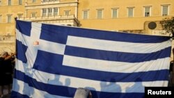 Des manifestants s'agenouent devant le drapeau grec à Athènes, Grèce, le 29 juin 2015.