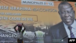 A girl stands next to a campaign poster of Cisse Ibrahima "Bacongo," a candidate for the municipal elections, on April 19, 2013 in Abidjan, two days ahead of the vote. 