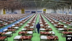 People in protective clothing walk past rows of beds at a temporary 2,000-bed hospital for COVID-19 coronavirus patients set up by the Iranian army at the international exhibition center in northern Tehran, Iran, on Thursday, March 26, 2020. (AP…