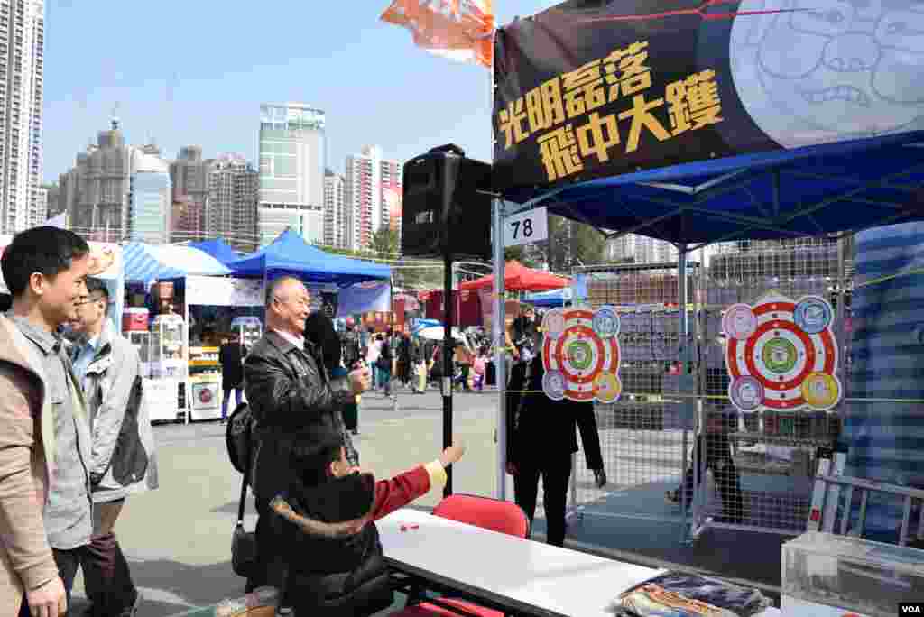 有家長帶同小朋友在香港工黨維園年宵市場的攤位，玩惡搞港府高官的飛標