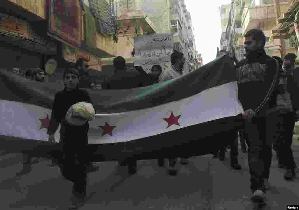 A boy holds bread as he walks in front of the Syrian opposition flag during a protest against Syria's president and Islamic State in Iraq and the Levant in Aleppo's Salaheddine neighborhood, Jan. 10, 2014. 