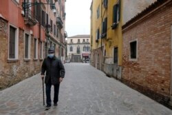 FILE - An elderly man with a protective mask walks in Venice, on the fourth day of a lockdown across Italy, imposed to slow the outbreak of coronavirus, March 13, 2020.