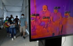 FILE - Visitors to Six Flag Fiesta Texas pass through a thermal screening area as they enter the park as a precaution against the coronavirus, June 19, 2020, in San Antonio.