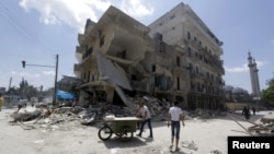A man pushes a cart near damaged buildings in Aleppo's al-Saliheen district, May 2, 2015. 