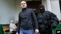 A police officer escorts Russian opposition leader Sergei Udaltsov, center, for questioning in Moscow, October 17, 2012.